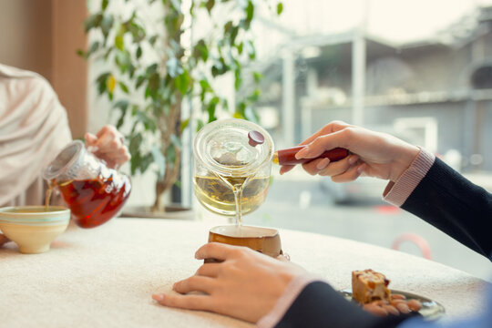 Close Up Female Hands Pouring Tea In Cup At Restaurant Or Cafe, Daily Lifestyle. Comfortable Atmosphere, Warm, Leisure, Drinks And Food. Friends, Family Or Business Meeting.