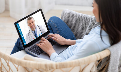 Telemedicine concept. Young lady consulting her doctor on laptop computer, using webcam from home,...