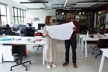 Diverse male and female colleague looking at blueprints and discussing