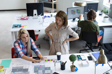 Two diverse businesswomen looking at blueprints and discussing in creative office