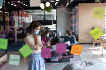 Asian businesswoman wearing face mask using tablet in creative office