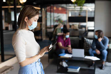 Asian businesswoman wearing face mask using tablet in creative office