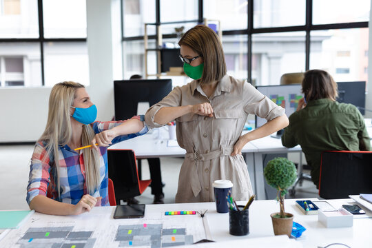 Two diverse businesswomen wearing face masks bumping elbows in creative office - Powered by Adobe
