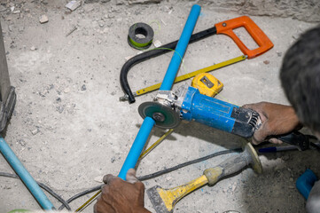 Plumber using electric saw cutting pvc pipe during renovation
