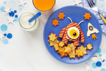 Cute smiling alien shaped hamburger served with roast potatoes, carrots and eggs for a healthy lunch or dinner with yoghurt and orange juice. Fun food for kids