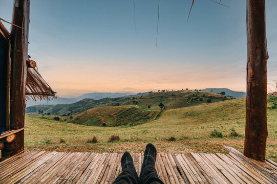 Legs of traveler relaxing in hut on green hill at sunrise