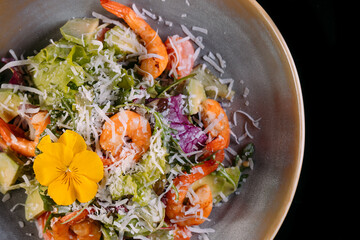 Seafood Caesar Salad with Shrimps, Salad Leaf, Croutons, Cherry Tomato and Parmesan Cheese on gray plate isolated on black background.Top view.