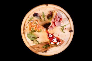 Assorted bruschetta with various toppings.Appetizing bruschetta.Variety of small sandwiches.Mix bruschetta with salmon, smoked meat, smoked tomatoes on wooden plate isolated on black background.