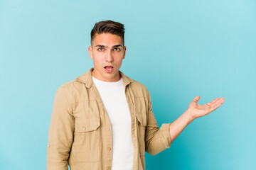 Young caucasian handsome man isolated impressed holding copy space on palm.