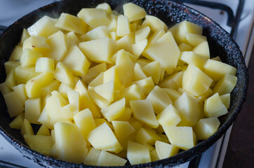 Chunks of peeled potatoes in a skillet on the kitchen stove.