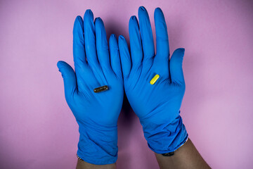 hands with blue latex gloves holding a yellow medicine pill in the palm with pink background