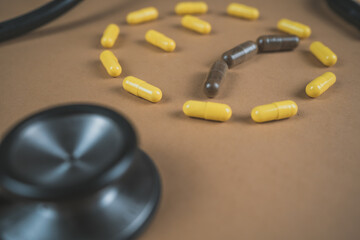 bottle of yellow and brown medicinal pills with phonendoscope on a beige brown background