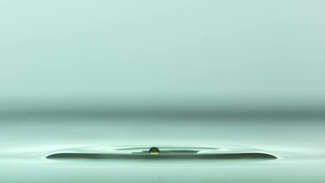 Close up of a yellow water droplet falling In teal water In super slow motion