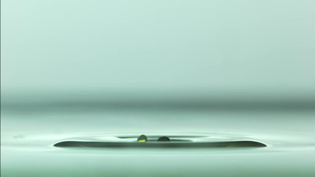 Close up of a yellow water droplet falling In teal water In super slow motion