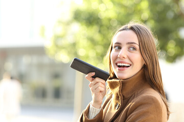 Happy woman dictating message on phone in winter