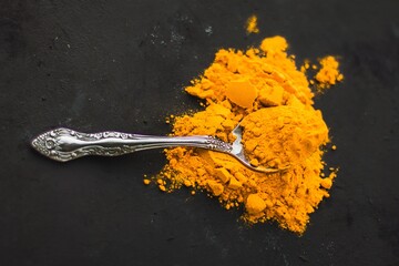 Spices turmeric in a spoon on a dark background, seasonings and healthy food