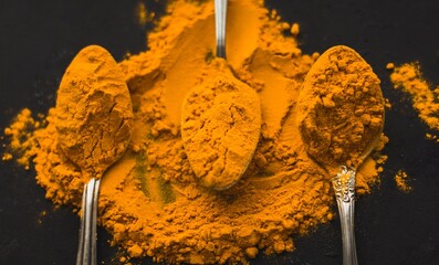 Spices turmeric in a spoon on a dark background, seasonings and herbs, natural medicine of India