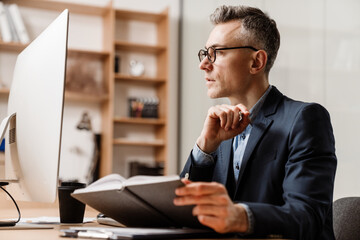 Serious grey man working with computer and planner in office