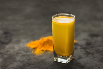 Turmeric latte, a golden milky hot healthy drink on a dark background in a glass tumbler - obrazy, fototapety, plakaty
