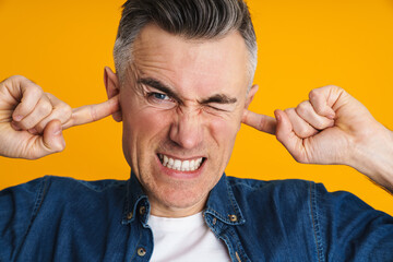 Displeased handsome man grimacing while plugging his ears