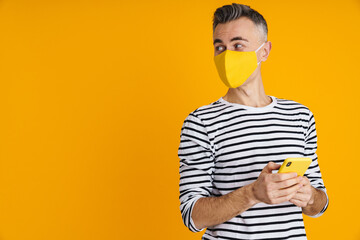 Pleased handsome man in protective mask using mobile phone