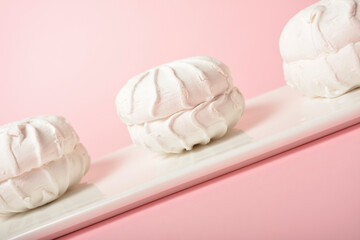 Three pieces of zefir sweet dessert served on white plate, isolated on colorful pastel pink background. Russian marshmallow made of egg whites, fruit paste and organic apple pectin. Selective Focus
