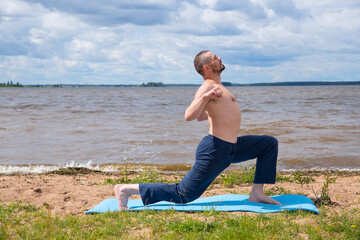 Man, 40 years old, European, doing yoga gymnastics on the seashore.