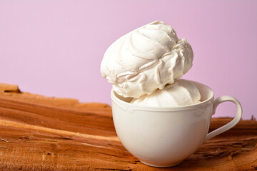 Vintage cup with two pieces of Russian traditional marshmallow dessert zefir (zephyr) souffle served on wooden log on violet background. Similarly with Meringue Dessert. Copy space image
