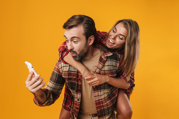 Excited man using cellphone while piggyback riding his smiling girlfriend