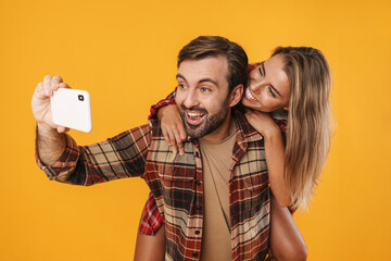 Excited man taking selfie on cellphone while piggyback riding his girlfriend