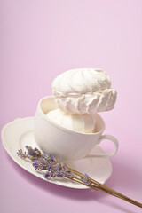 Vintage cup with two pieces of Russian traditional marshmallow dessert zefir (zephyr) souffle served with lavender herbs on plate isolated on violet background. Similarly with Meringue Dessert
