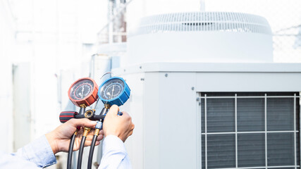 Air repair mechanic using measuring equipment for filling industrial factory air conditioners and...