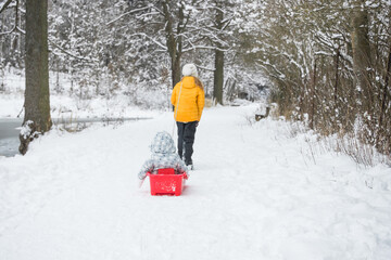 Young girl drag little baby on plastic sled, back view.