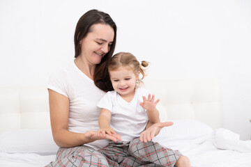 adult mother play with little active daughter in bed at home, having fun, activity with children.