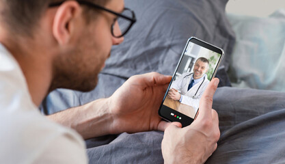 Young man having online consultation with doctor on smartphone, using telemedicine app on bed, panorama
