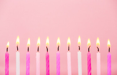 Various pink color birthday cake candles burning in line on pastel pink background, studio shot,...
