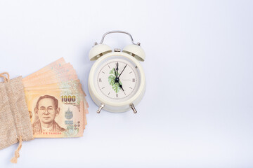 Many baht piles in sacks and alarm clocks are separated on a white background, used for money-saving results idea