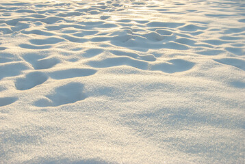 Snow drifts illuminated by the sun, human footprints in the snow. Abstract background. Space for copying.