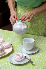 Red-manicured hands hold a white teapot before pouring tea into a cup. Selective focus.