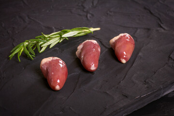 Fresh raw chicken hearts on a black board with a sprig of rosemary. Chicken offal. Top view