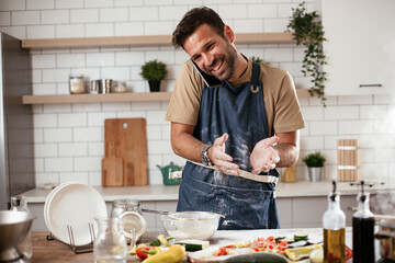 Fototapeta na wymiar Attractive man cooking in modern kitchen. Handsome man talking to the phone while cooking..