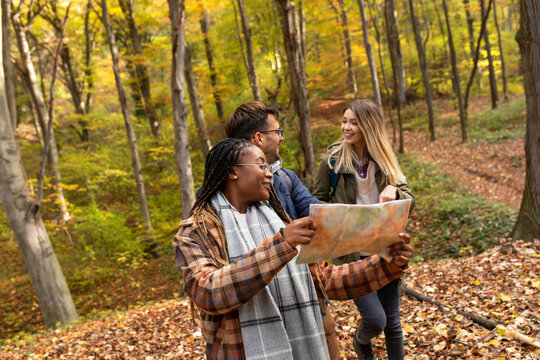 Happy group of friends with map hiking through forest