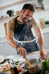 Attractive man cooking in modern kitchen. Handsome man talking to the phone while cooking..