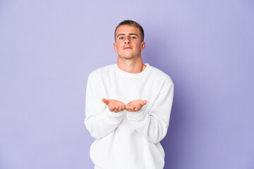 Young caucasian handsome man holding something with palms, offering to camera.