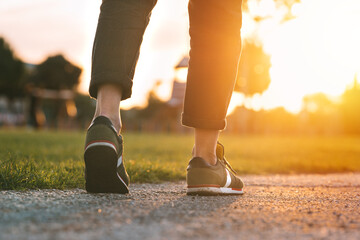 Woman walking in the park at sunset. Closeup on shoe with rolled up jeans. Taking a step. Woman on...