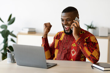 Overjoyed African Businessman In Traditional Clothes Celebrating Success At Workplace In Office