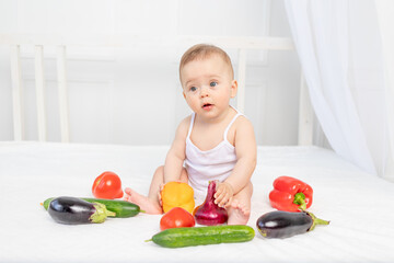 Obraz na płótnie Canvas little baby sitting on the bed in the nursery with vegetables, baby food concept,