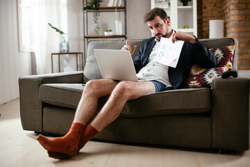 Businessman working online, wearing suit and no pants. Young man having video call. Businessman working at home