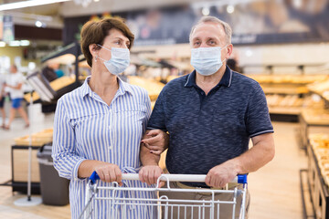 Man and woman in protective masks with shopping cart in supermarket