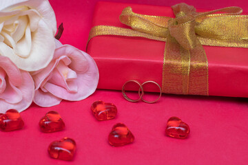 Preparation for the wedding: two rings, flowers, a gift box and hearts on a red background. The photo